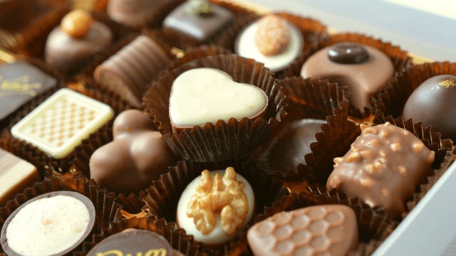 A box of assorted chocolates, including heart-shaped, nut-topped, and variously textured pieces arranged in paper liners, perfect for celebrating Valentines in Japan with a touch of sweetness.