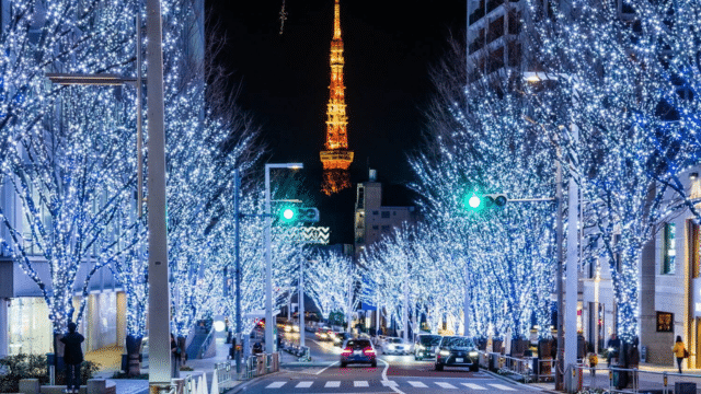 An illuminated street, perfect for a romantic stroll during Valentines in Japan, is lined with trees adorned in blue lights, leading to a lit-up tower glowing softly in the night.