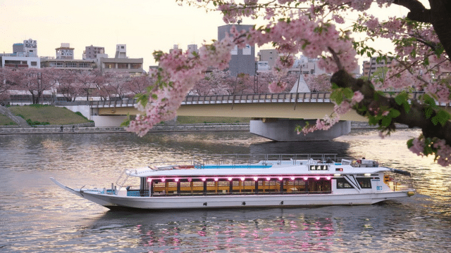 A boat drifts along a river beneath a bridge, with pink cherry blossoms framing the scene—a picturesque moment perfect for celebrating Valentines in Japan.