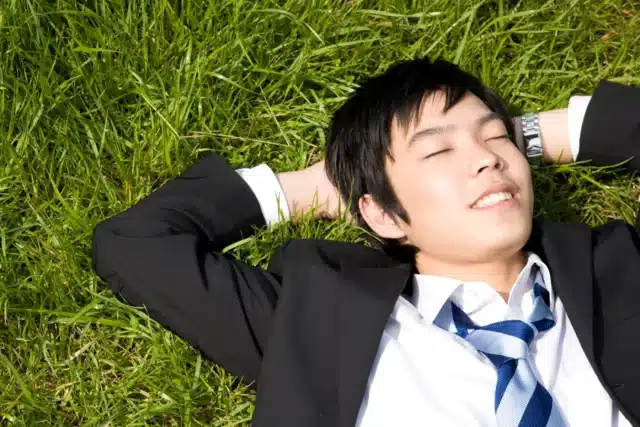 A person in a suit and tie lies on green grass with eyes closed and hands behind their head, appearing relaxed—an ideal moment that could inspire a thoughtful gift for boyfriend who deserves some downtime.