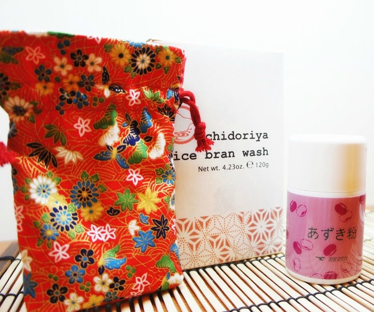 Colorful drawstring pouch, a box labeled "Chidoriya Rice Bran Wash," and a small white container with Japanese text sit on a bamboo mat, perfect for your next beauty event.