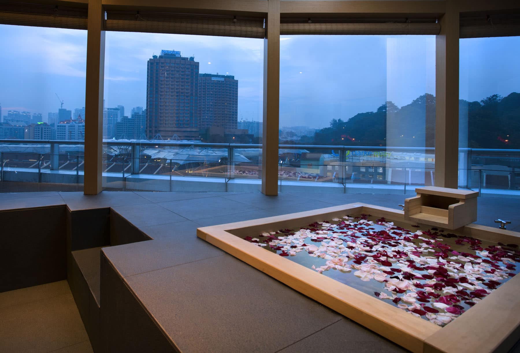 A Japanese spa experience featuring a bathtub adorned with rose petals, offering a view of the cityscape.