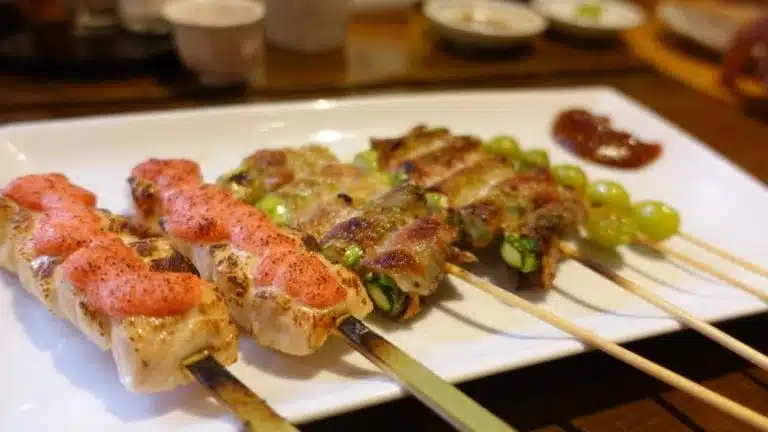 A white plate with several grilled skewers, each topped with different ingredients, is served on a table with sauce on the side—perfect for enjoying during a Tokyo solo holiday.