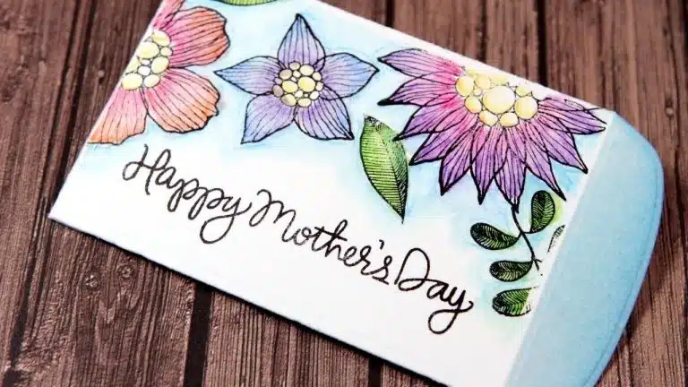 A card with colourful hand-drawn flowers and the text "Happy Mother’s Day" on a wooden surface, perfect as a thoughtful Mother’s Day gift.