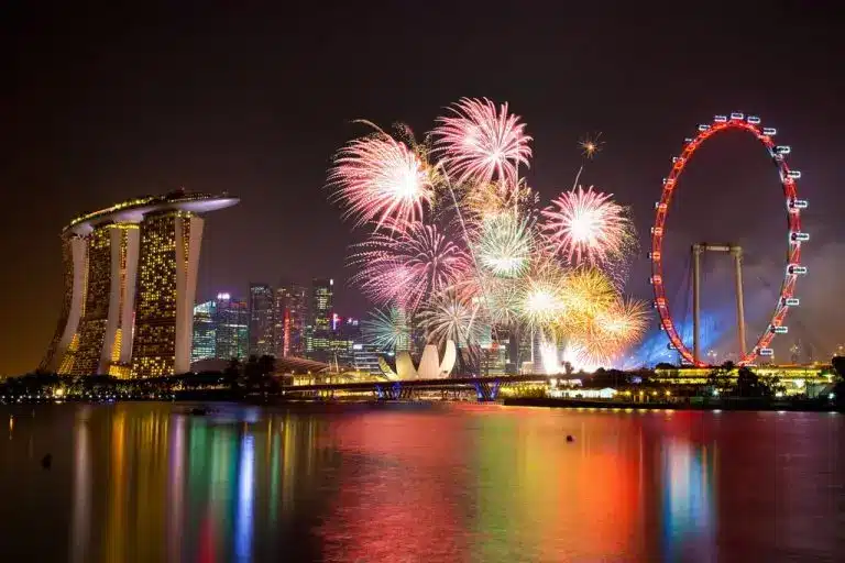 NDP Fireworks light up the night sky over Marina Bay in Singapore, with the Singapore Flyer and city skyline reflected in the water.