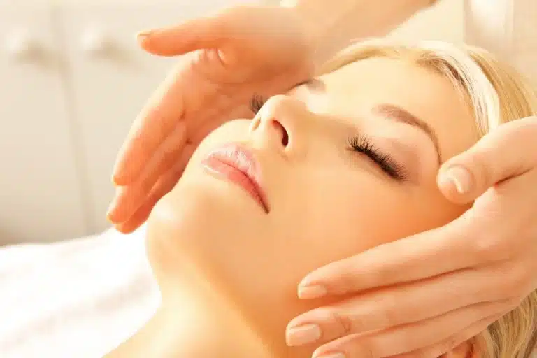 A person with closed eyes receives a facial massage, as skilled hands practise massage therapy around their face in a relaxing spa setting.