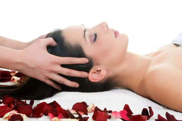 Person lying on a towel with eyes closed, enjoying soothing Massage Therapy as rose petals are scattered on the towel around the head.