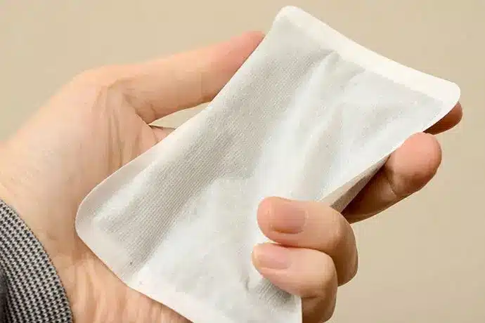 A hand holding a rectangular disposable heat pack with a white fabric exterior, showing how to keep warm in winter.