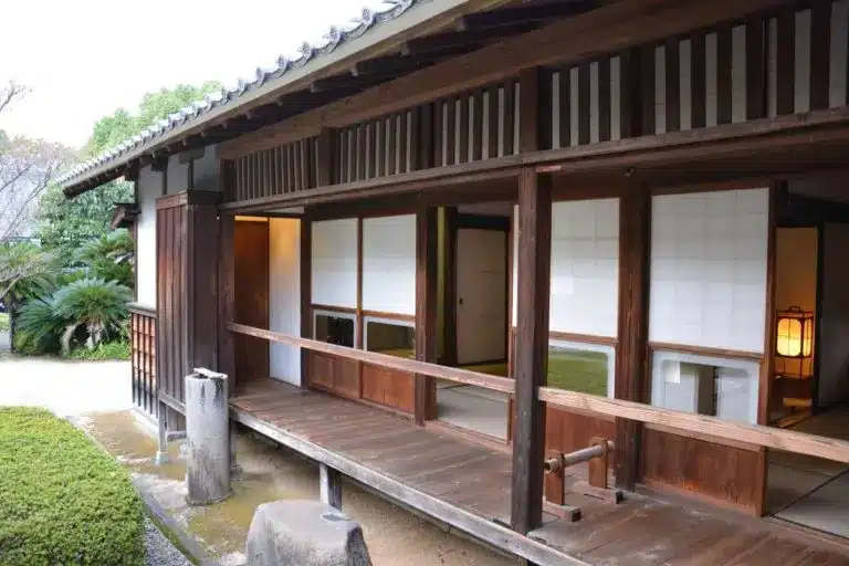 Traditional Japanese wooden house with sliding shoji doors, a covered verandah, and a landscaped garden visible in the background—showcasing time-honoured ways on how to keep body warm in winter.