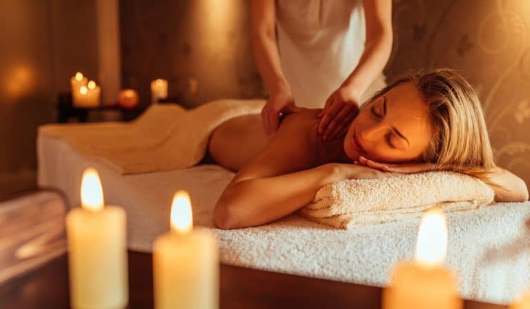 A woman lies on a spa bed receiving a back massage. There are lit candles in the foreground, creating a relaxing atmosphere often associated with massages in Singapore.