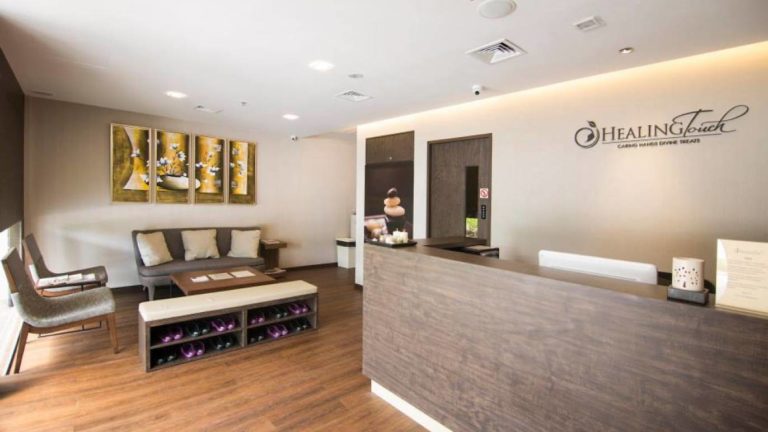 A modern spa reception area with a desk, couch, chairs, artwork, and a sign that reads "Healing Touch," welcoming guests for the best massages in Singapore.