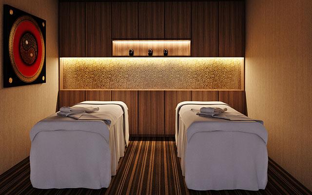 A serene room with two side-by-side massage tables, soft lighting, wooden paneling, striped flooring, and a decorative wall piece—perfect for indulging in massages in Singapore.