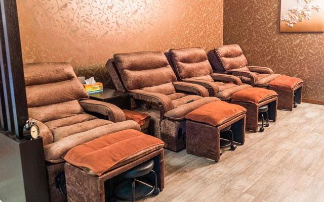 A row of brown, cushioned massage chairs with leg rests in a room with patterned wallpaper and tiled flooring offers one of the best massages in Singapore.