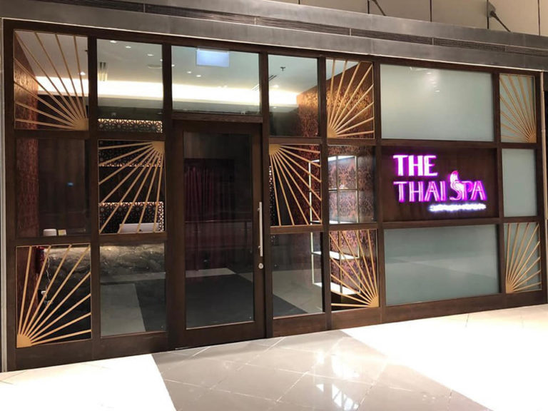 Exterior of "THE THAI SPA" with a neon sign and Art Deco style metal and glass facade, offering an oasis of relaxation with the finest massages in Singapore.