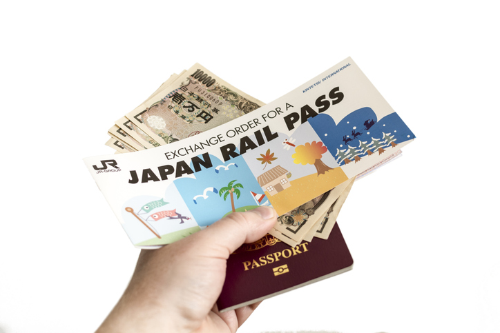 A hand holding Japanese yen, a JR Pass exchange order, and a passport against a white background.