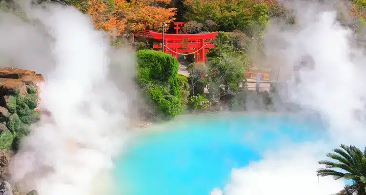 A hot spring pool with steaming water, surrounded by green foliage and a red torii gate in the background, is just one of Japan's serene spots accessible with a JR Pass.