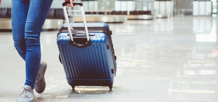 A person walks through an airport terminal pulling a blue wheeled suitcase