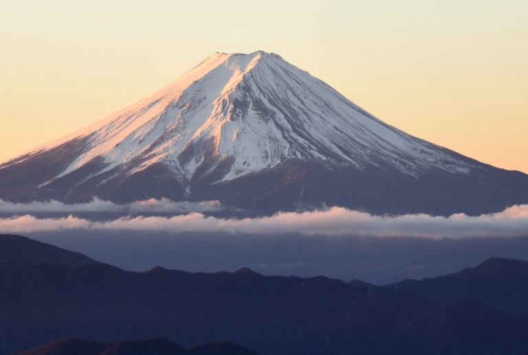 A snow-capped mountain peak rises above a layer of clouds with a clear sky in the background, offering breathtaking scenery to travelers exploring Japan with their JR Pass.