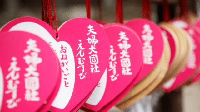Heart-shaped ema plaques with Japanese writing, hanging on strings at a Shinto shrine, create a picturesque scene that's especially charming around White Day.