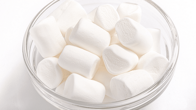 A clear glass bowl filled with white, cylindrical marshmallows, perfect for celebrating White Day.