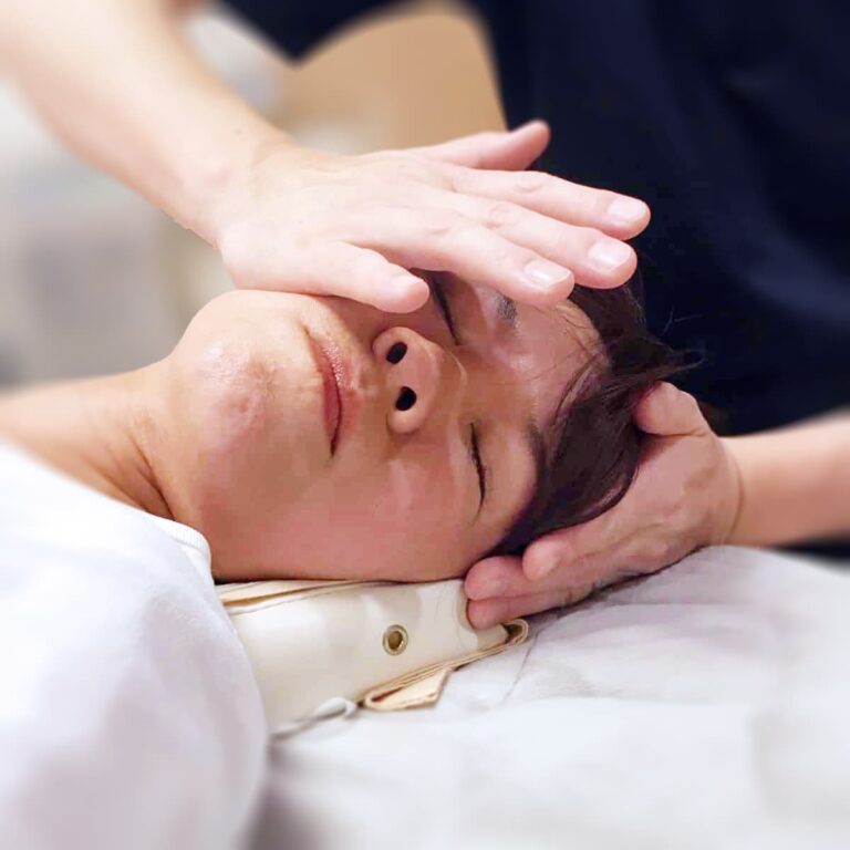 Close-up of a person receiving a gentle massage on the forehead and temples, focusing on kogao small face therapy, while lying down with eyes closed.