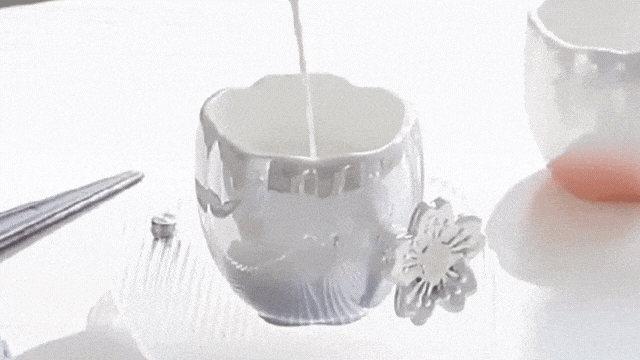 In a serene setting perfect for a spring spa promotion, a ceramic cup with silver glaze and delicate flower detail is gently filled with milk under soft lighting.