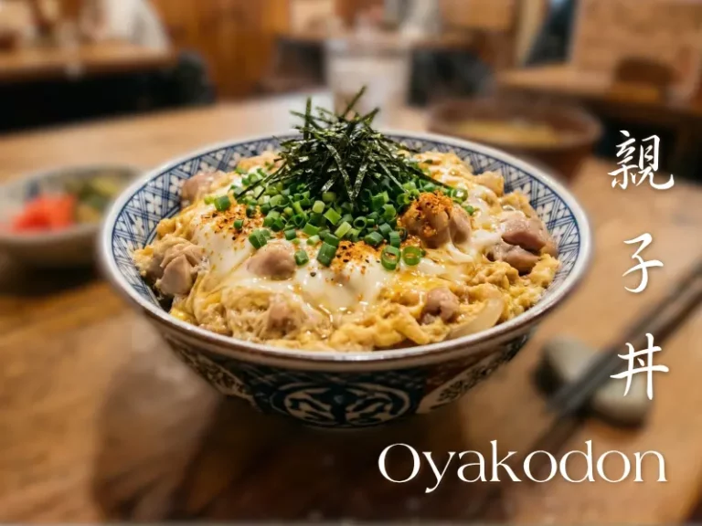 A bowl of oyakodon, a Japanese rice dish topped with chicken, egg, spring onions, and shredded nori, is placed on a wooden table.