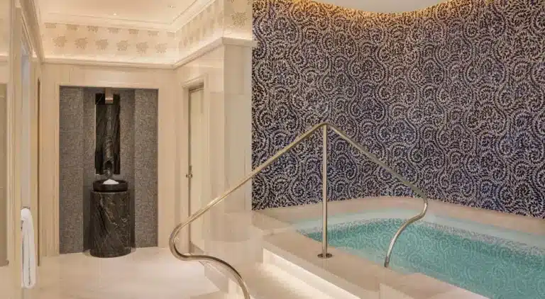 Luxurious indoor plunge pool with ornate blue and white tiled wall, gold handrail, and marble fountain feature in an elegant, well-lit room—perfect for relaxation after a massage Singapore experience.