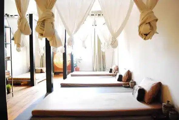 A room with several floor mattresses, pillows, and draped white fabric hanging from the ceiling, creating a serene and minimalist atmosphere reminiscent of a tranquil massage Singapore retreat.