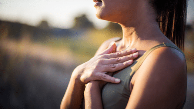 A person outdoors places both hands on their chest, wearing a sleeveless top, perhaps finding solace in nature as part of their insomnia treatment, with a blurred background.