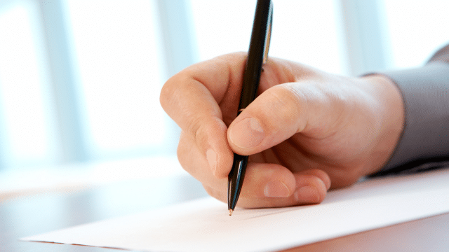 Close-up of a hand holding a pen, writing on a sheet of paper.