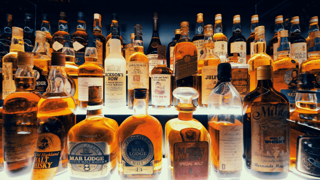 A collection of various whiskey bottles, with different shapes and labels, displayed on illuminated shelves.