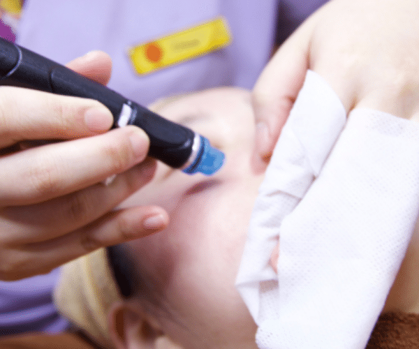 A person indulges in a Hydrafacial treatment, with a handheld device gently gliding over their skin, while a soft cloth drapes over part of their face.