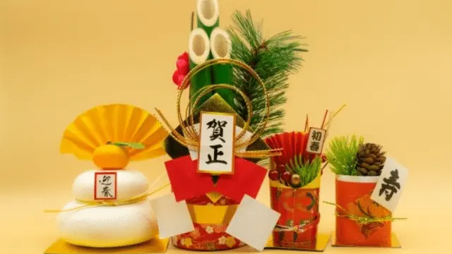 Traditional Japanese New Year decorations, featuring a kagami mochi, kadomatsu, and festive ornaments, evoke the spirit of both Chinese New Year and Japan against a plain yellow background.