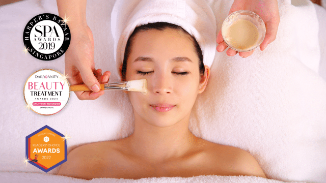 Amidst the serene aura of a spa, a person lies on a bed with a towel draped over their head, indulging in a luxurious facial treatment with a brush.