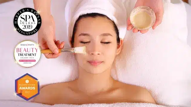 A person with a towel wrapped around their head receives a facial mask treatment, evoking the relaxation of Chinese New Year spa rituals in Japan. Several beauty and spa award badges are displayed on the image.