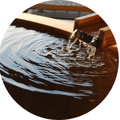 Water flowing from a wooden spout into a pool creates soothing ripples, reminiscent of the tranquility found in an onsen facial experience.