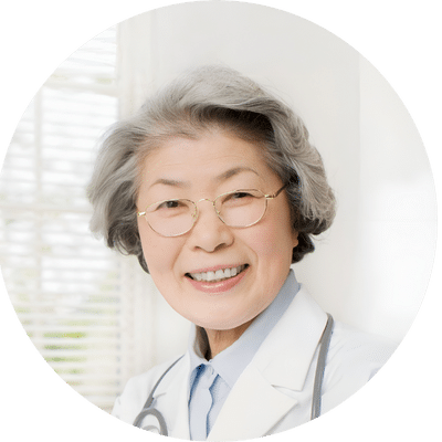 Smiling older woman in a white coat with glasses and gray hair, standing indoors near a window, radiating the serene glow of an onsen facial.