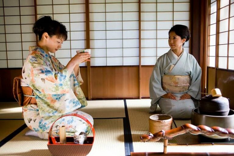 Two people in traditional Japanese attire participate in an elegant Japanese tea ceremony, surrounded by tatami mats and shoji screens. One gracefully pours tea while the other observes with appreciation.