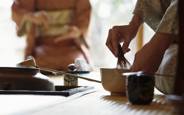 A person in traditional attire gracefully prepares matcha tea with a whisk, embodying the elegance and ritual of the Japanese tea ceremony.
