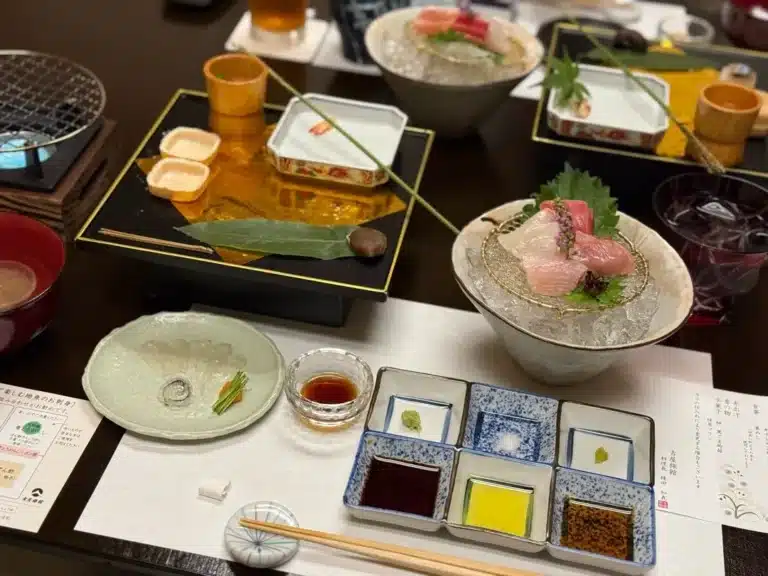 A traditional Japanese meal with assorted sashimi on ice, dipping sauces in square dishes, small appetisers, and garnish, arranged neatly on a table—perfect after a relaxing day at an onsen Singapore experience.