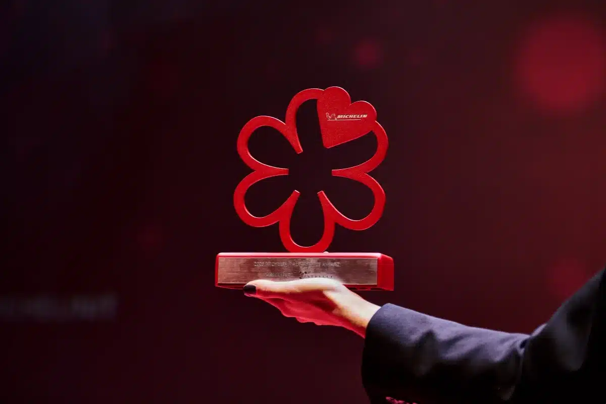 A person holds a red Michelin Guide award shaped like a stylised flower against a dark blurred background, celebrating the achievement of a renowned Japanese restaurant in Singapore.