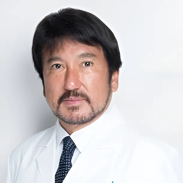 A man with short dark hair and a beard, wearing a white lab coat and a dark patterned tie, poses against a plain light background.