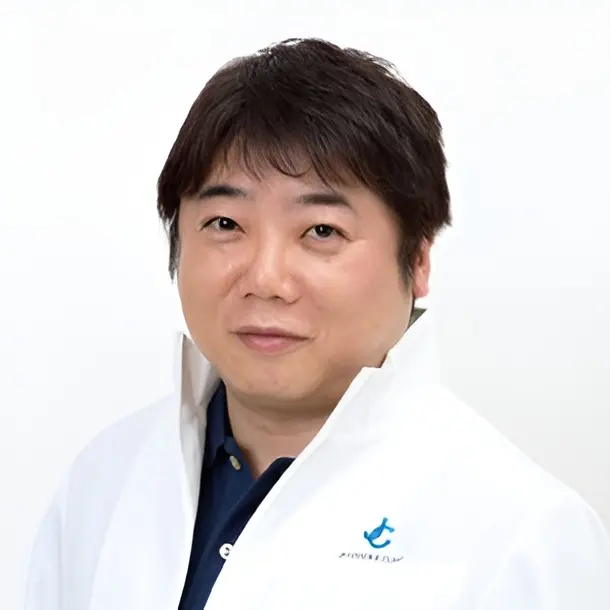 A man with short dark hair wearing a white jacket over a dark shirt poses in front of a plain white background.