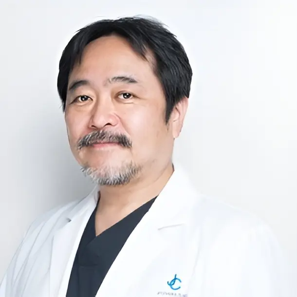 A middle-aged man with short dark hair and a mustache, wearing a white lab coat and dark shirt, stands against a plain light background.