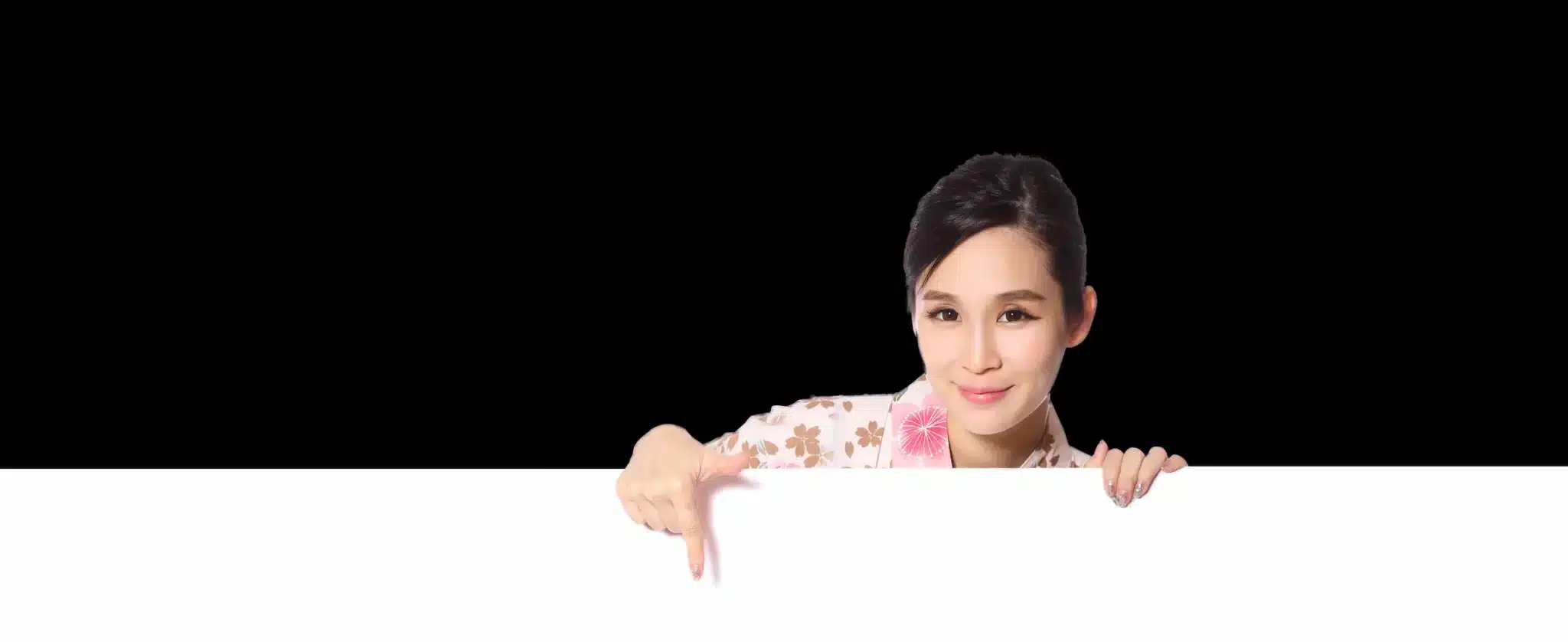 Woman with dark hair wearing a floral top points down at a blank white sign against a black background.