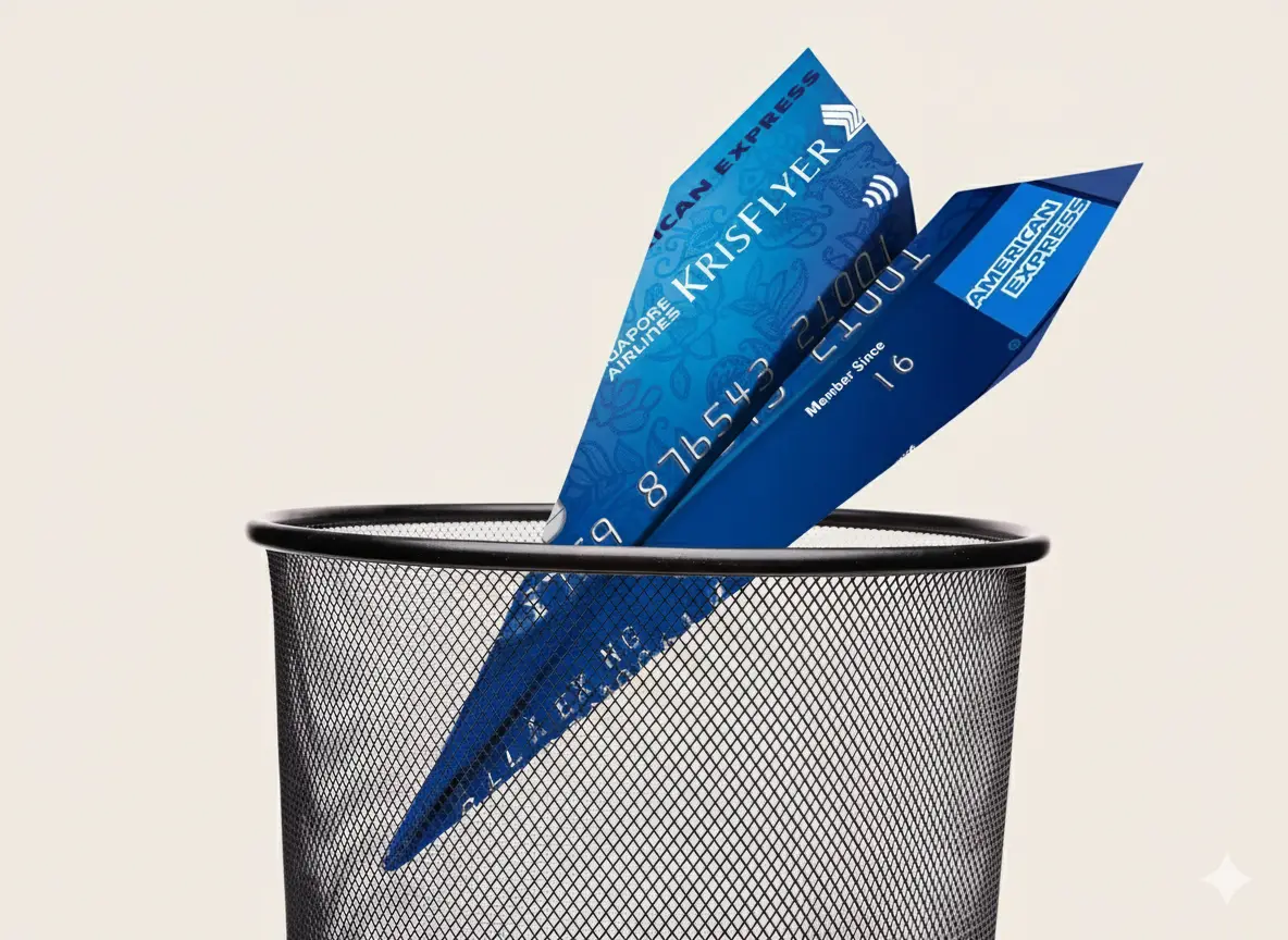 A blue credit card folded into a paper airplane sits in a mesh trash bin against a plain background.