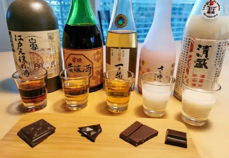 Four bottles of sake and four filled glasses are lined up on a table, each paired with a piece of dark chocolate in front of them.