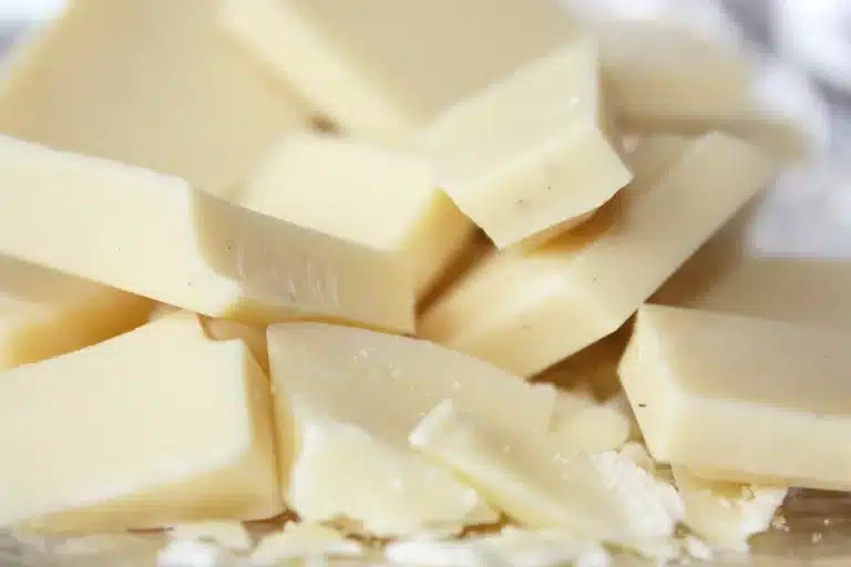 Close-up of several pieces of white chocolate stacked together on a surface, perfect for a unique sake chocolate pairing or to enjoy alongside a sake Kit Kat, with some small flakes and crumbs scattered around.