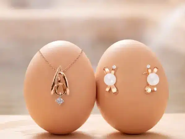 Two brown eggs are displayed upright; one is adorned with a gold necklace and the other with matching pearl and gold earrings